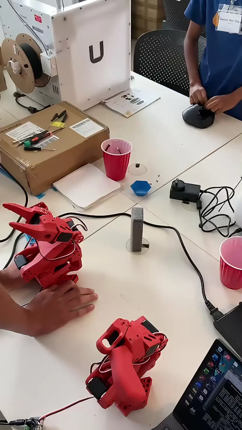 Two red SO-101 robot arms on the MakerLab worktable
